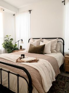 a bed with white sheets and pillows in a bedroom next to two plants on the nightstands