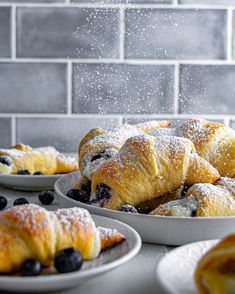 blueberry croissants on white plates with powdered sugar falling over them