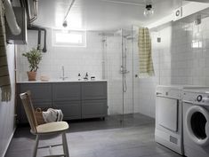 a washer and dryer in a bathroom with white tiles on the walls, along with a wooden chair