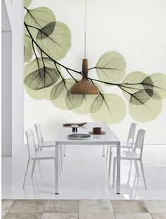 a white table with chairs and a lamp hanging from it's centerpiece in front of a leafy wall mural