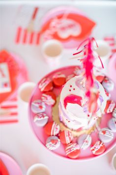 a cupcake on a pink plate surrounded by other plates and napkins with hearts