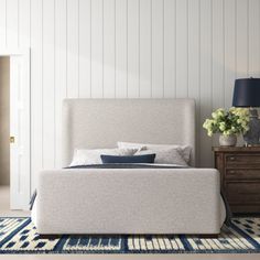 a white bed sitting on top of a blue rug next to a dresser and lamp