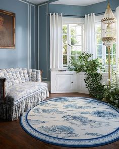 a living room with blue walls and white curtains on the windowsills, a round rug in front of a window