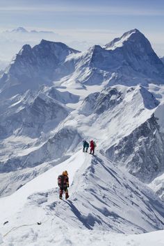 three people climbing up the side of a snow covered mountain with mountains in the background