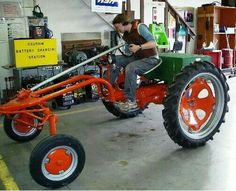 a man riding on the back of an orange and green tractor in a garage next to other tools