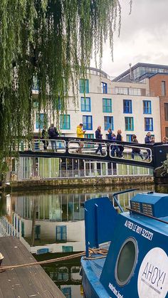 people are walking on a bridge over the water in front of some buildings and boats