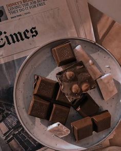 some pieces of chocolate sitting on top of a plate next to a newspaper and cup