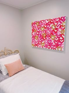 a white bed topped with a pink and yellow painting next to a wall mounted art