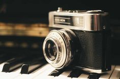 an old fashioned camera sitting on top of a piano keyboard with the keys still attached