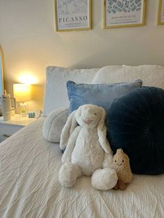 two stuffed animals sitting on top of a bed next to pillows and lamps in a bedroom