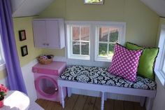 a small room with a window seat and pink play table in the corner next to it