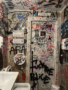 a bathroom with graffiti all over the walls and on the door, there is a sink