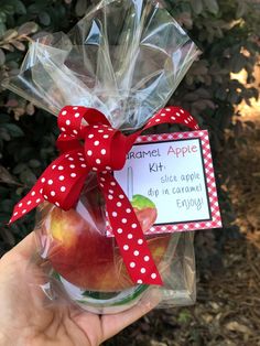 a hand holding an apple in a jar with a red bow and label on it