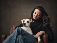 a woman sitting in a chair with her dog on her lap and looking at the camera