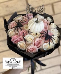 a bouquet of roses and white pumpkins is held by a person's hand