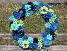 a wreath made out of blue and green flowers sitting on top of a wooden bench