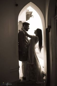 a man and woman standing next to each other in front of a doorway with an arch