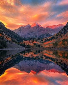 the mountains are reflected in the still water at sunset, with red and yellow clouds