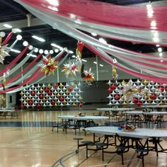 an indoor banquet hall decorated with red, white and gold balloons and streamers on the ceiling