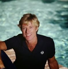 a man sitting in front of a swimming pool with his hand on his hip and smiling