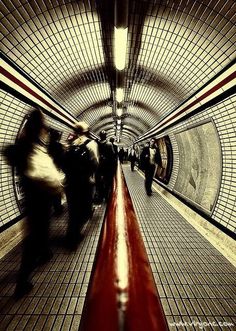 people are walking through a subway tunnel with tile flooring and red railings on either side