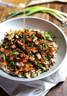 a white bowl filled with rice and vegetables on top of a wooden table next to asparagus