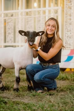 a woman kneeling down next to a sheep on top of a grass covered field in front of a building