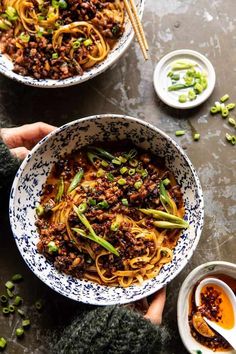 two bowls filled with noodles and vegetables next to dipping sauces on a table top