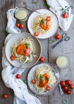 two plates of spaghetti with tomato sauce and tomatoes on the table next to glasses of milk