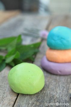 three different colored doughnuts sitting on top of a wooden table next to green leaves