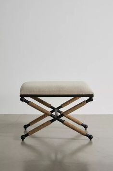 an upholstered bench with black legs and a beige seat cushion on top of it