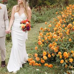 a bride and groom holding hands in front of orange flowers on their wedding day at the farm