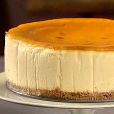 a cheesecake sitting on top of a white cake plate covered in caramel sauce