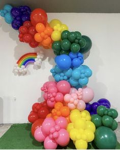 balloons are arranged in the shape of a rainbow on a green carpeted floor next to a white wall