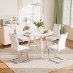 a white table and chairs in a room with hardwood floors, windows, and rugs