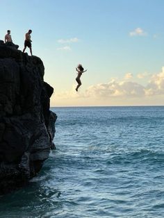 two people jumping off rocks into the ocean from a rocky cliff in front of them