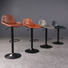 three different colored barstools sitting next to each other in front of a gray wall