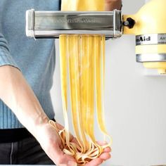 a person is holding some noodles in front of a yellow machine with it's hands