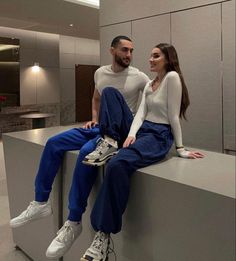 a man and woman sitting on top of a counter next to each other