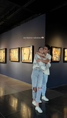 two people hugging each other in front of paintings on the wall at an art gallery