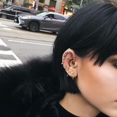 a woman with black hair wearing ear piercings on her ears and looking off to the side