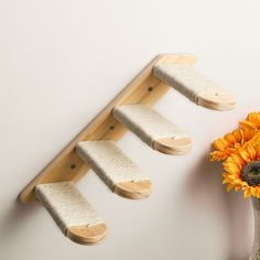 a vase with sunflowers and three wooden pegs on it next to a wall