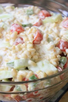 a glass bowl filled with pasta salad on top of a wooden table next to a red and white checkered napkin