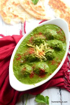 a white bowl filled with green soup next to bread