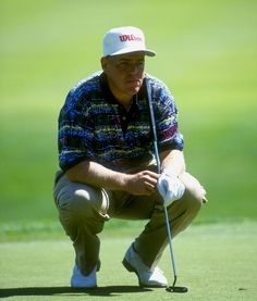 an older man kneeling down to put his golf ball on the green while wearing a hat