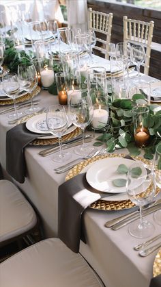 the table is set with white and gold plates, silverware, candles and greenery