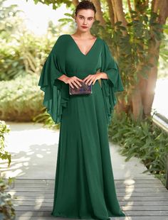 a woman in a green dress standing on a wooden walkway with trees and bushes behind her