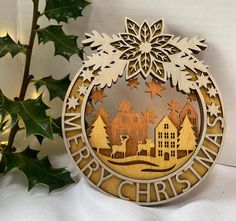 a wooden christmas ornament with the words merry christmas written in gold and surrounded by holly leaves