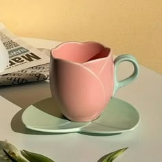 a pink coffee cup sitting on top of a saucer next to a paper bag