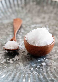 a wooden spoon filled with white sugar on top of a metal plate next to a scoop of sea salt